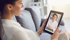 Woman sits on a couch with her tablet during a mental health visit